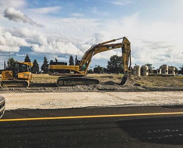 A yellow excavator and bulldozer working on graded ground beside a newly surfaced road.